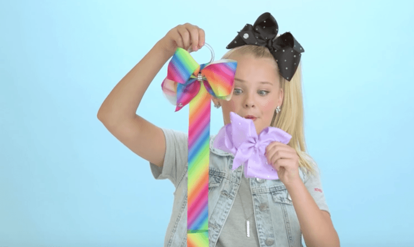 Girl wearing black polka dot JoJo Siwa Bow holding rainbow and purple JoJo Siwa bows, LuvHer Shop