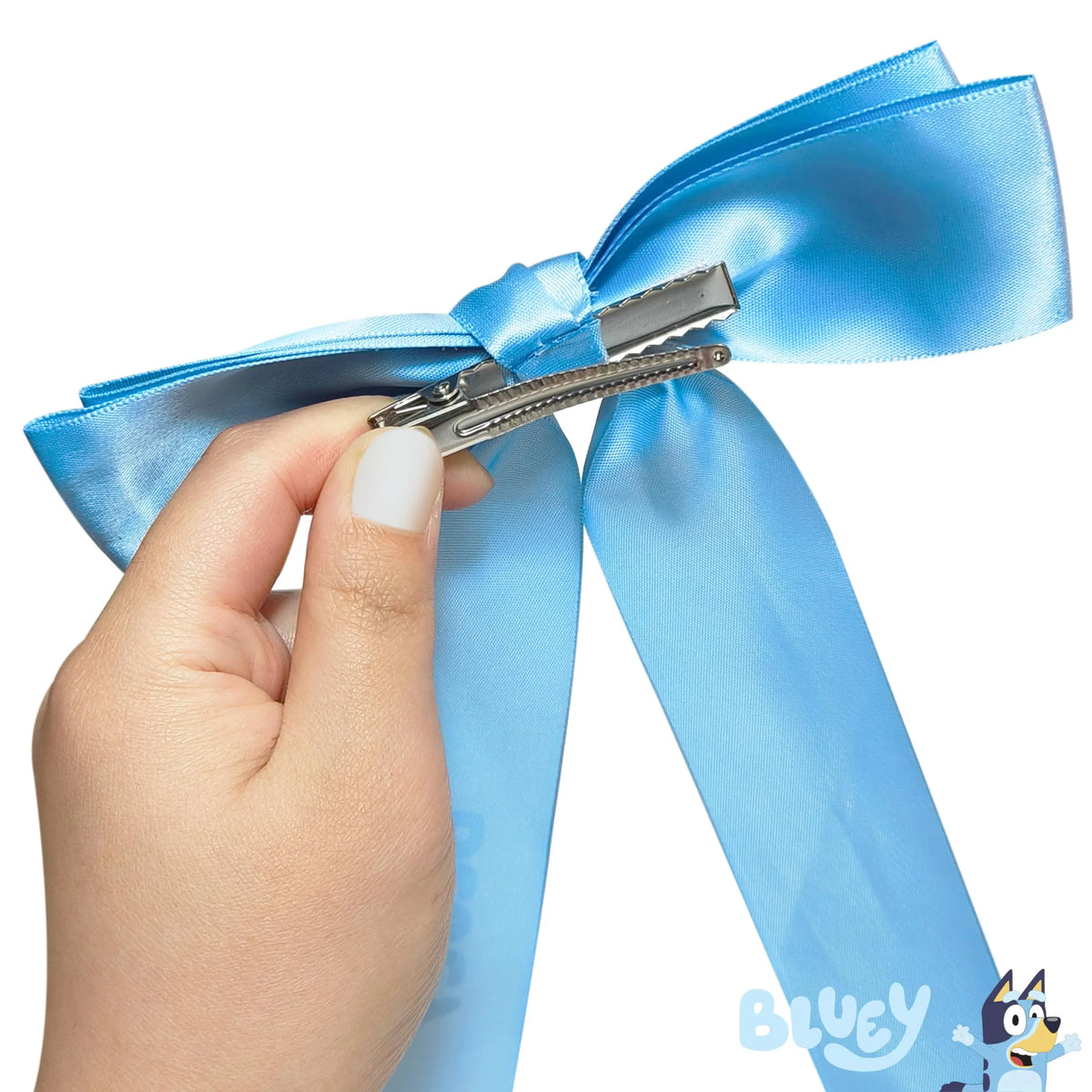 Hand holding Bluey Bow hair clip, featuring light blue satin ribbon with Bluey logo.