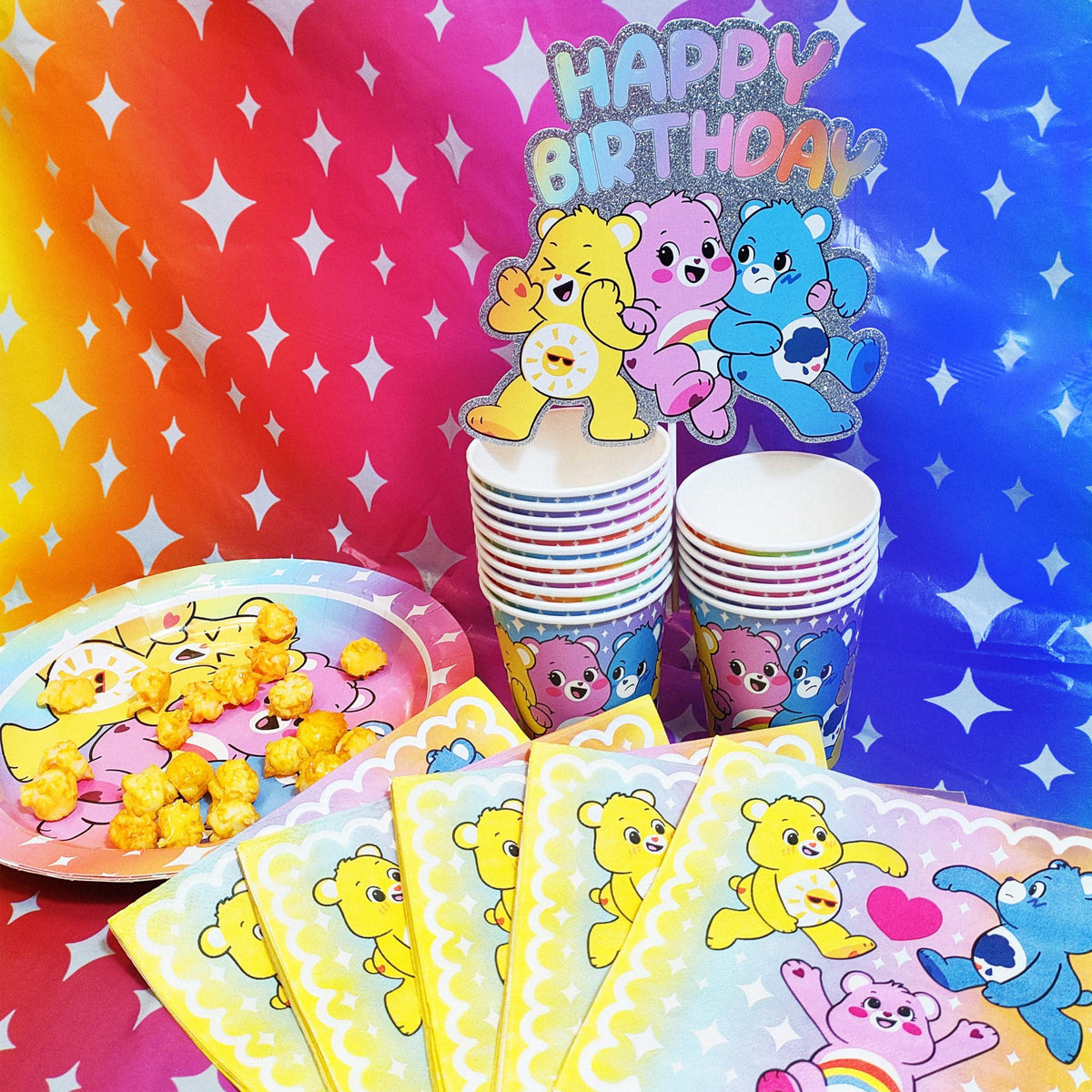 Care Bears birthday party supplies set with colorful cups, napkins, and plates on rainbow background